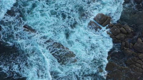 Top-aerial-drone-view-of-waves-crashing-on-rocky-coastline