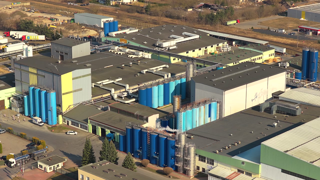 Drone footage of a large dairy product manufacturing plant in grajewo, poland. Industrial buildings with blue silos and trucks in the parking lot