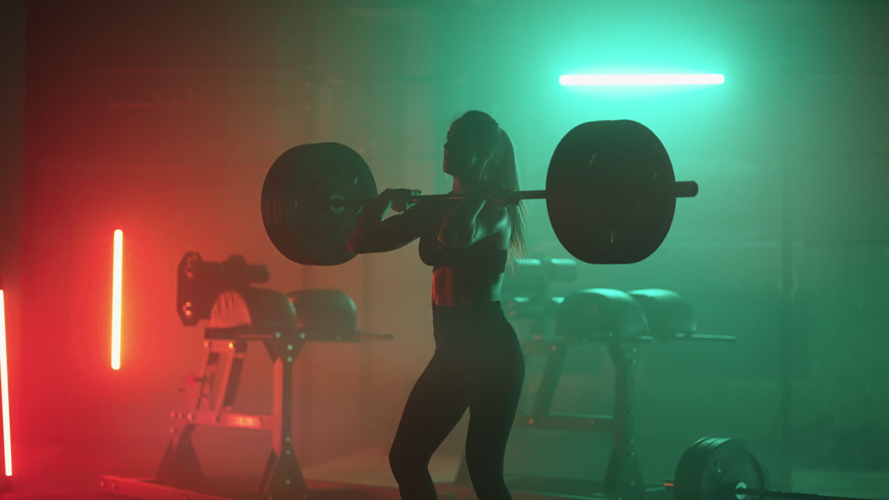 강력한 여성은 체육관에서 바벨을 들어 올리고 있습니다. 체력을 유지하기 위해 파워 리프팅과 보디 빌딩 훈련