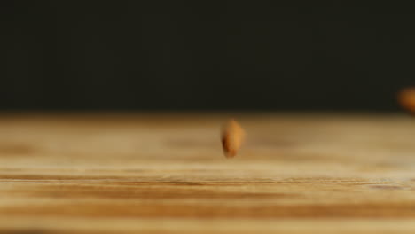 close up shot of almond nuts dropping onto wooden surface against black studio background shot in slow motion