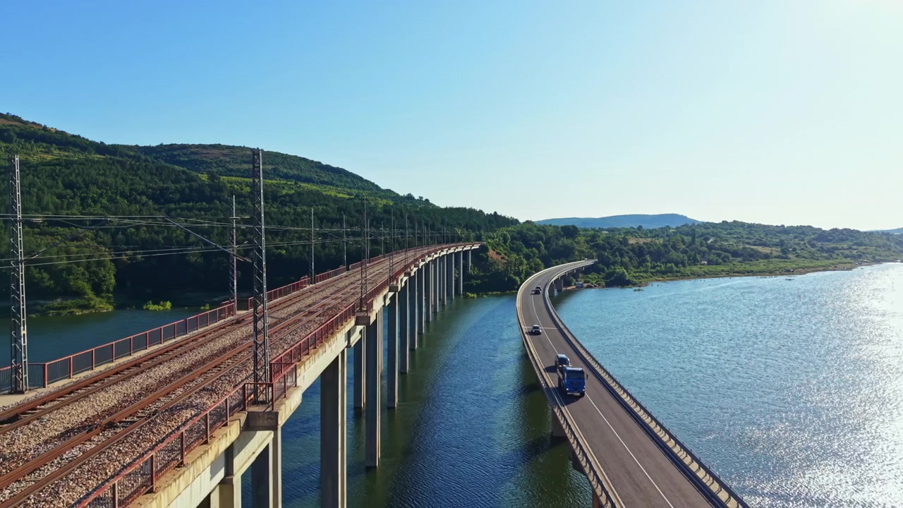 Ponte ferroviario e stradale sopra l'acqua vicino a colline in una giornata di sole