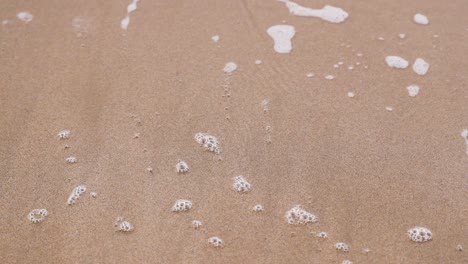 waves retreating, leaving bubbles on sandy shore