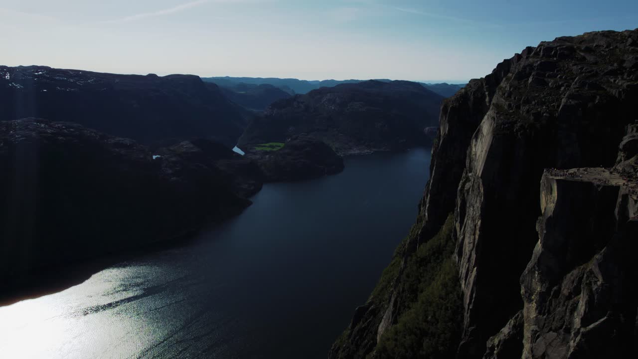 Wide aerial view of Preikestolen flat top rock with green valleys and blue fjord beyond in Norway.