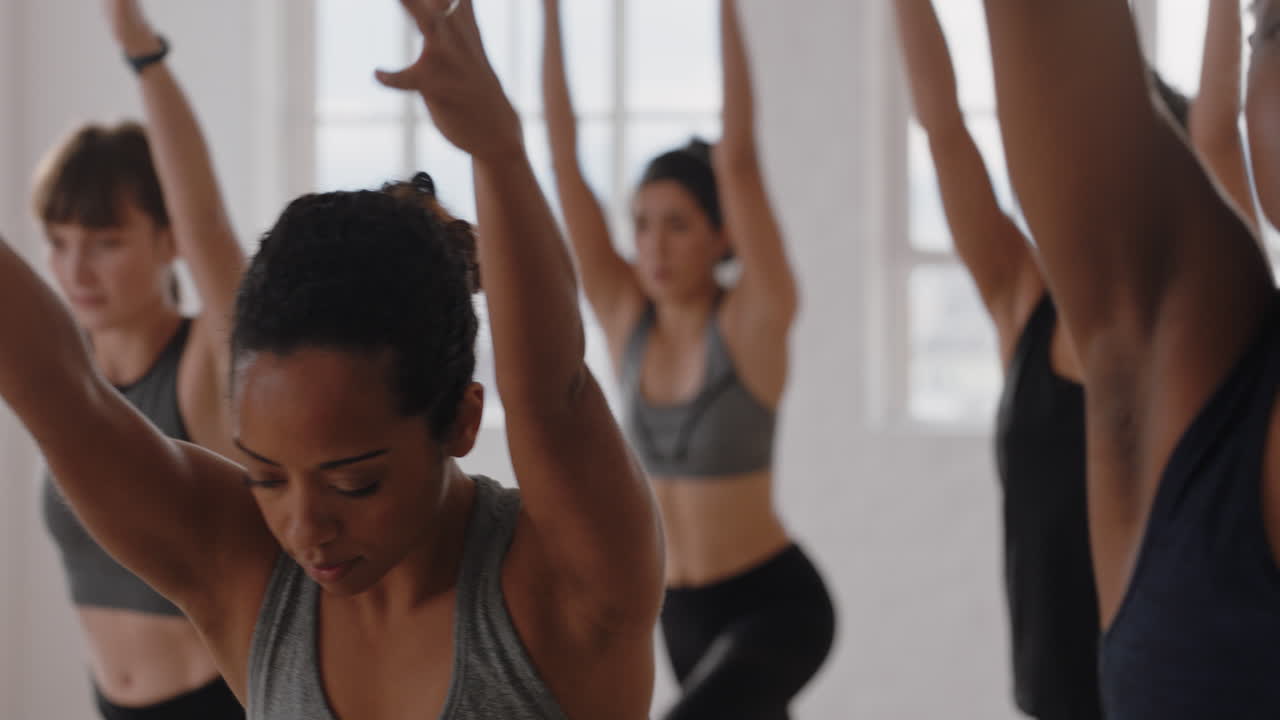 beautiful mixed race yoga woman practicing warrior pose meditation with group of multiracial women enjoying healthy lifestyle exercising in fitness studio