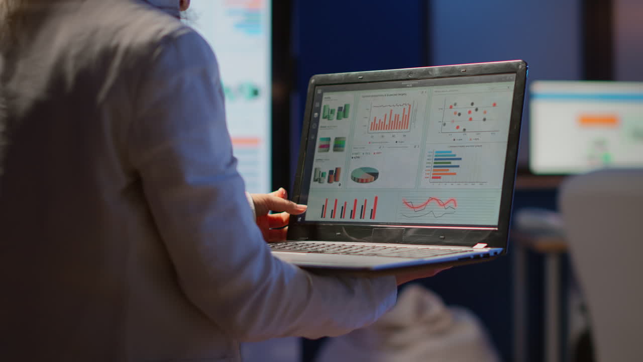 vista trasera de una mujer de negocios analizando estadísticas financieras con una computadora portátil