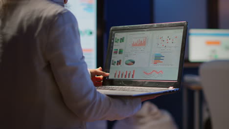 Back-view-of-business-woman-analysing-financial-statistics-holding-laptop