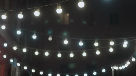 una acogedora escena al aire libre de la noche con luces de cuerda iluminando un camino alineado con bancos y una pared de ladrillo