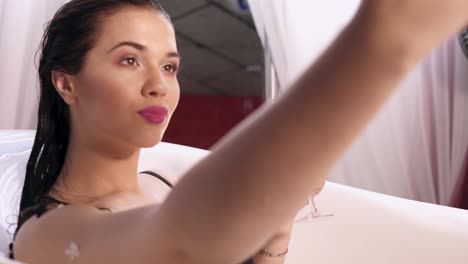 hermosa joven tomando una selfie relajándose en un baño de leche y bebiendo vino espumoso de un vaso. filmado en 4k
