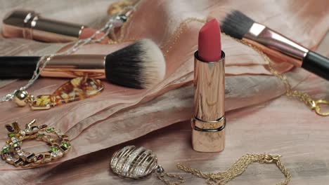 pan shot of a luxurious beauty setup featuring lipstick, makeup brushes, and gold jewelry on soft silk fabric, capturing a glamorous getting-ready moment