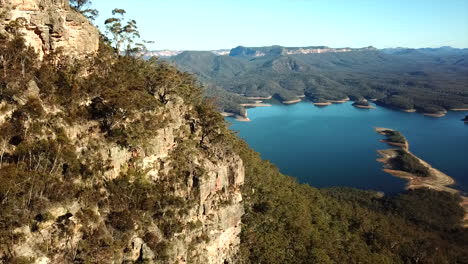 aerial: drone stationary pan past a mountain to a large beautiful blue lake surrounded by trees in new south wales, australia