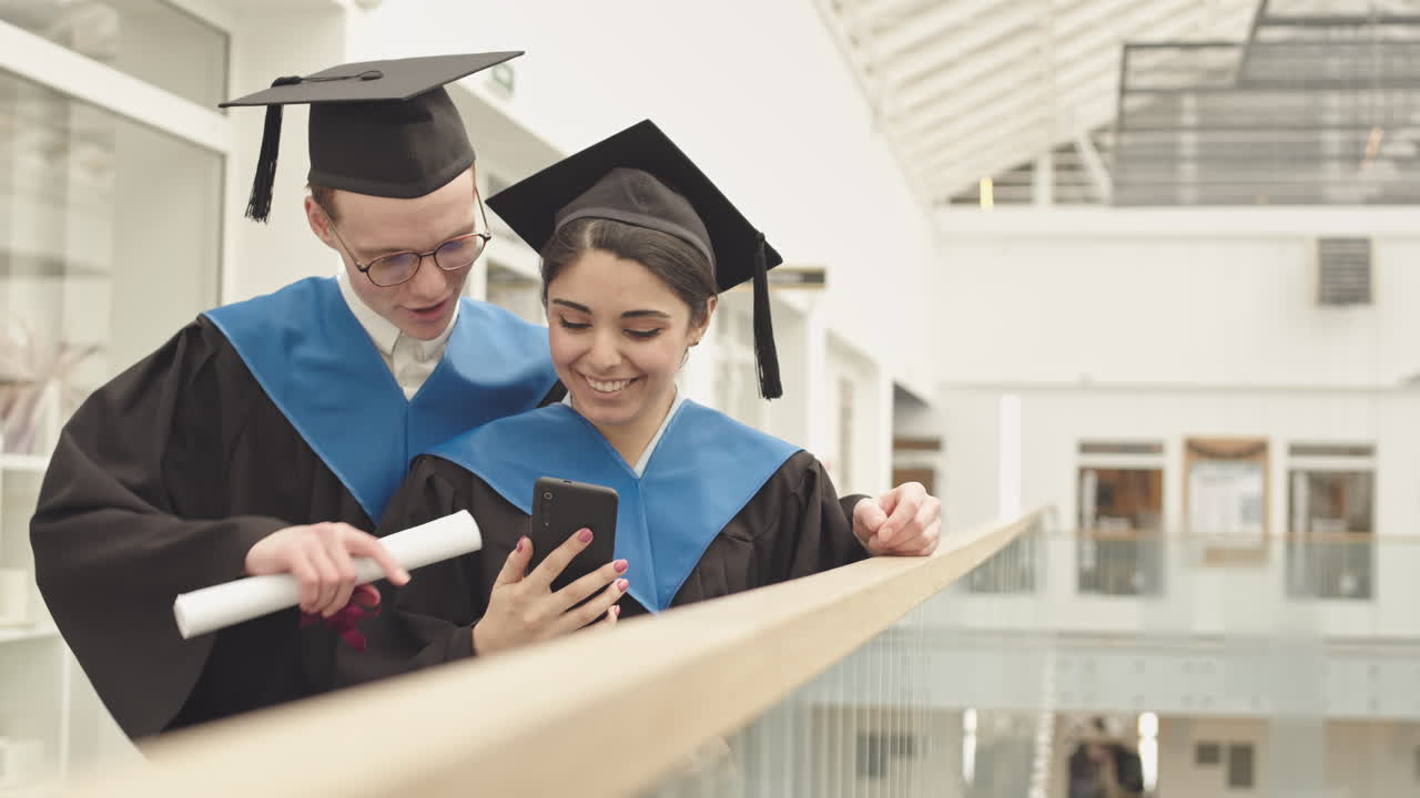 Two Joyful Diverse Graduates Using Cellphone