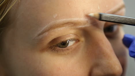 cosmetologist preparing young woman for permanent eyebrow make up procedure in beauty salon