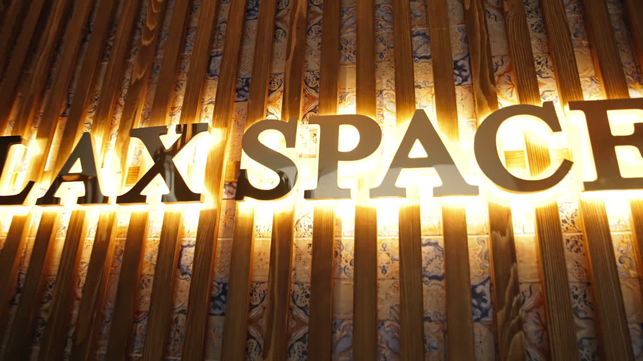 Signboard on the wall with beautiful golden letters lit brightly from behind. Name brand of a spa resort centre on the wooden panels.