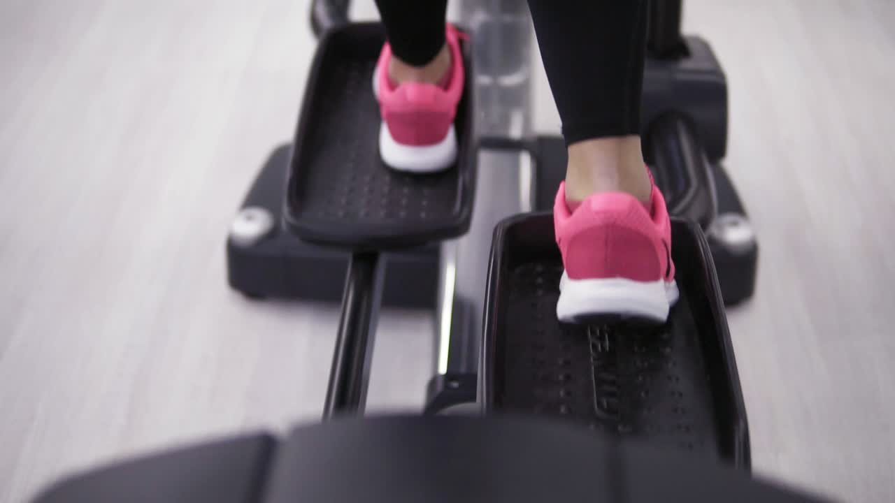 Female legs in pink sneakers pedaling on an orbitrek-simulator close up