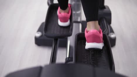 piernas femeninas en zapatillas rosadas pedaleando en un orbitrek-simulador de cerca