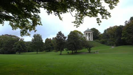 Idyllic-view-through-the-popular-Englischer-Garten-of-Munich,-the-green-park-with-an-unrecognizable-woman-enjoying-her-walk-with-a-dog-and-her-bike