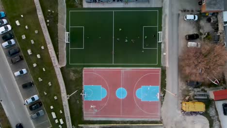 drone flight from bird's eye view over a small soccer field next to an basketball field where a game is being played