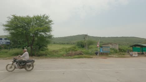 Side-angle-of-a-vehicle-passing-through-national-highway-with-visible-mountain-range-and-city-name-boards