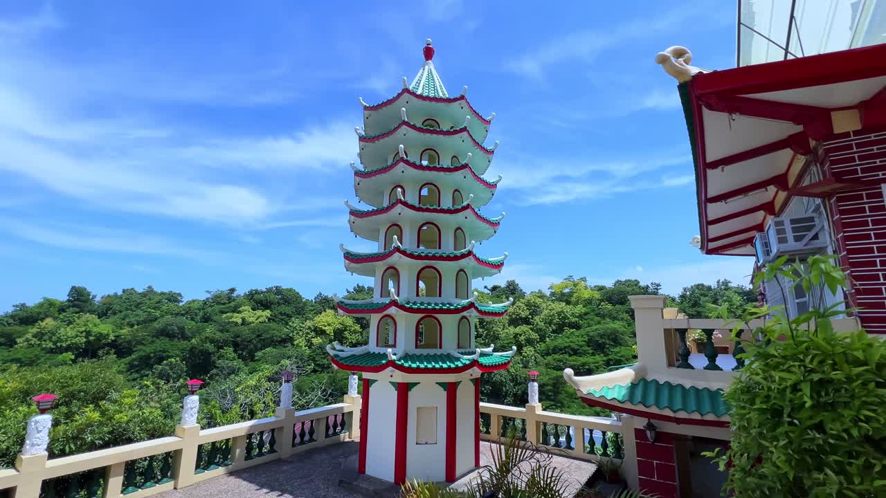 A vibrant Chinese-style pagoda stands tall against a bright blue sky, surrounded by tropical greenery. Ideal for travel, culture, and religion-related content