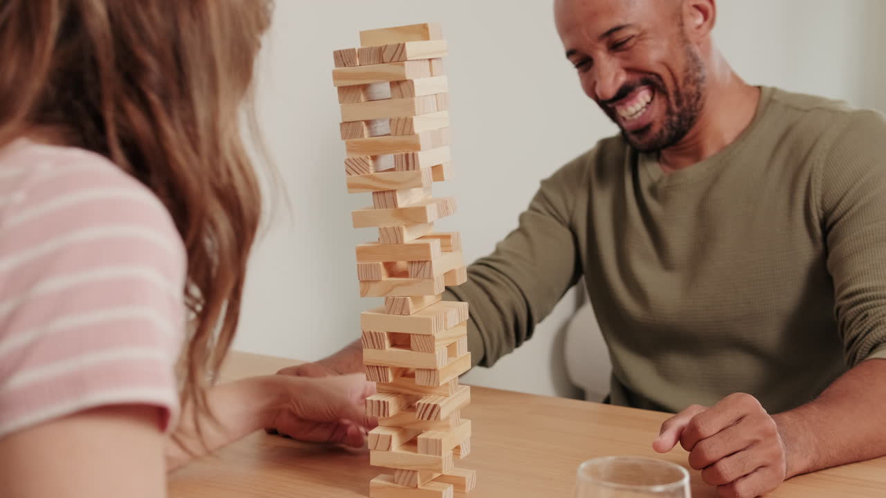 A mixed-race couple playing board games, playing Jenga and Laughing at Home