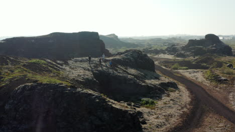 Drone-view-orbit-around-group-of-tourist-enjoying-panorama-climbing-hill-rock-formation-in-Iceland.-Aerial-view-turning-around-male-explorer-discovering-amazing-in-nature