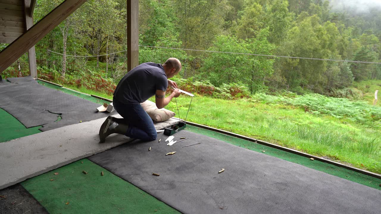 Man på skjutbana monterar en ballistisk precisionskronograf för att testa kulhastighet – Tomma mässingshylsor på marken och grön skogsbakgrund.