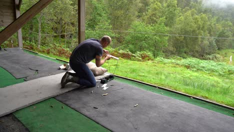 man at shooting range assembles ballistic precision chronograph for testing bullet speed - empty brass shells on ground and green forest background