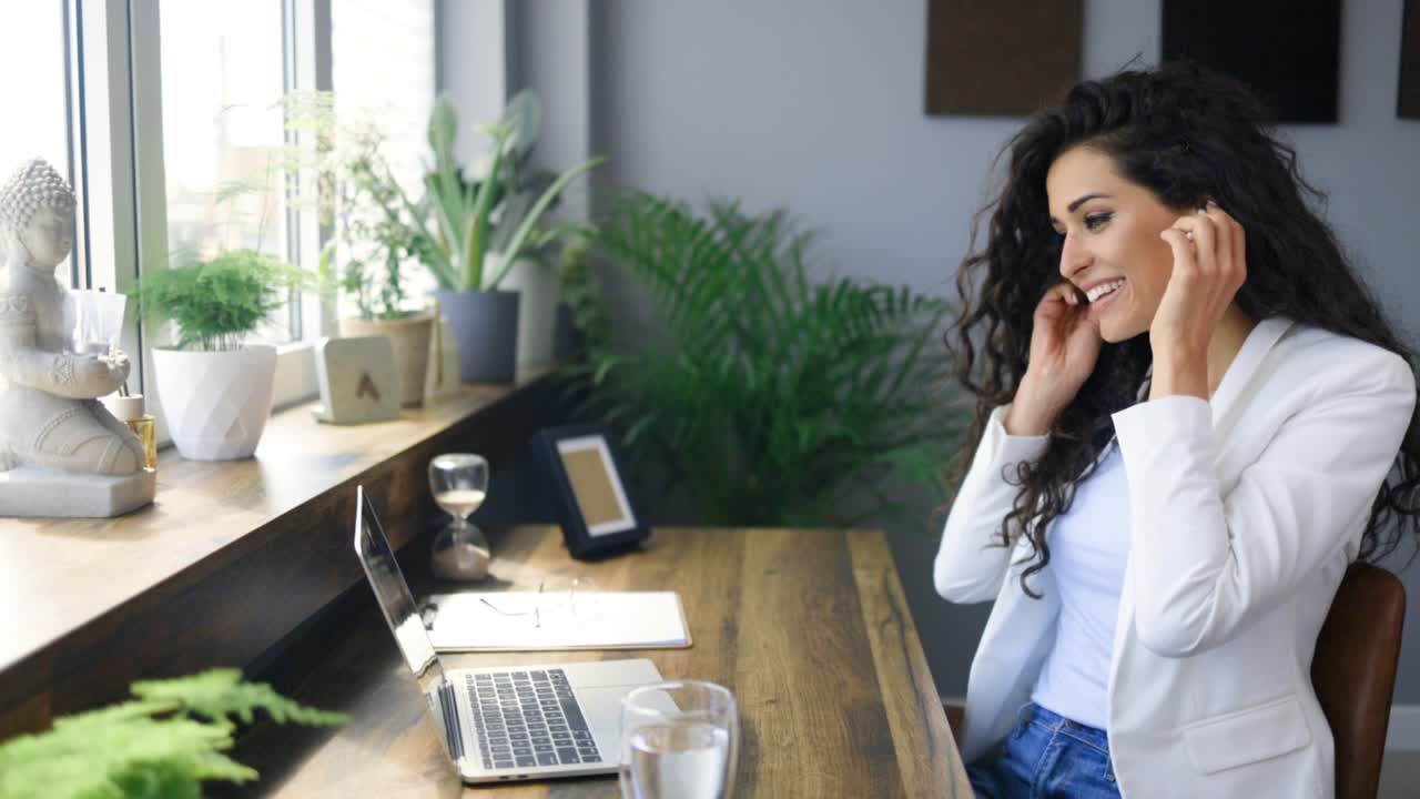 una mujer joven trabajando en una computadora portátil y refrescándose con un vaso de agua.