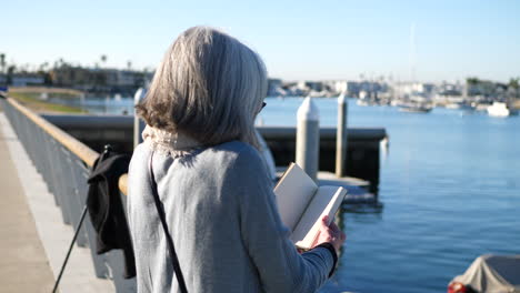 a beautiful old woman author looking at the pages of a blank book or journal as she thinks about what to write on the beach