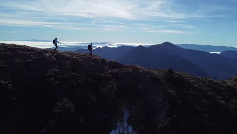 drone footage of two hikers walking on the edge in the mountains