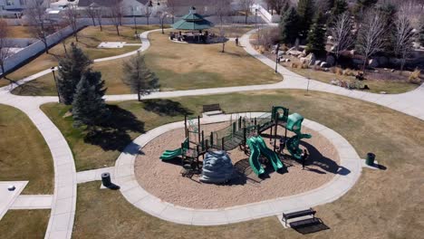 drone shot flying in counter clockwise circle over a public park with children’s playground, revealing houses and upper middle income american neighborhood