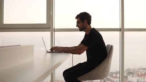 side view of business man using laptop computer at remote workplace in slow motion. freelancer working on computer at home. focused man looking laptop at big house with panoramic windows