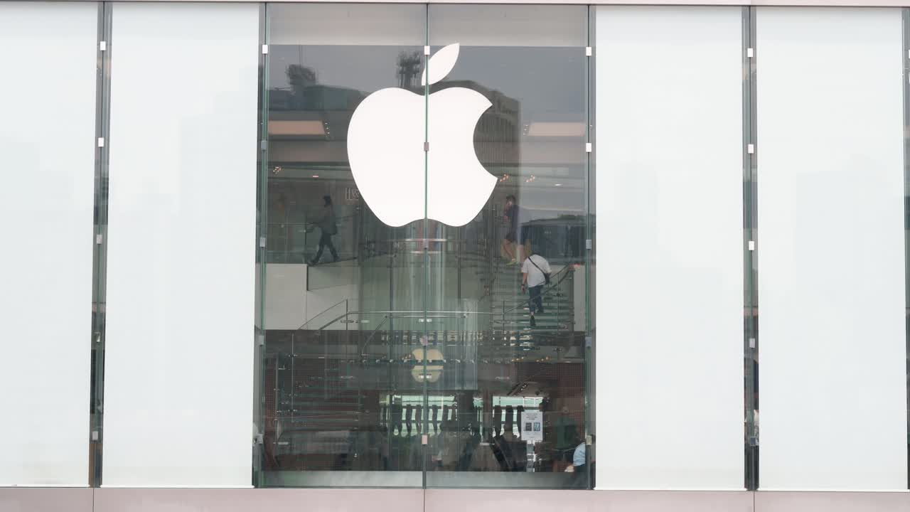 An exterior view of the Apple Store, showing customers ascending the staircase, with the company logo prominently displayed.