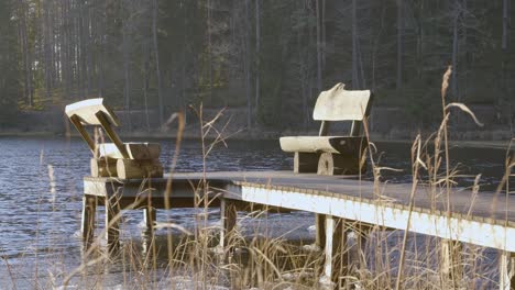 Close-up-of-vacant-wooden-benches-at-end-of-wooden-pier-beside-calm-beautiful-lake-during-sunny-day