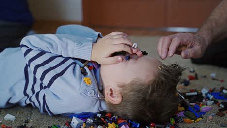 family playing with constructor. close up view of falling lego on small boy indoor