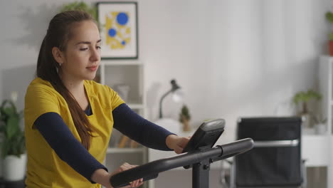joven mujer morena está entrenando con bicicleta estacionaria en casa medio retrato de persona girando pedales estilo de vida saludable
