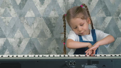 Kleines-Mädchen-Mit-Zöpfen-Spielt-Musiksynthesizer-In-Der-Nähe-Der-Wand