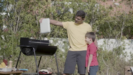 man standing with son at barbeque grill and waving lid