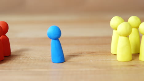 blue figurine standing between a group of red and yellow figurines