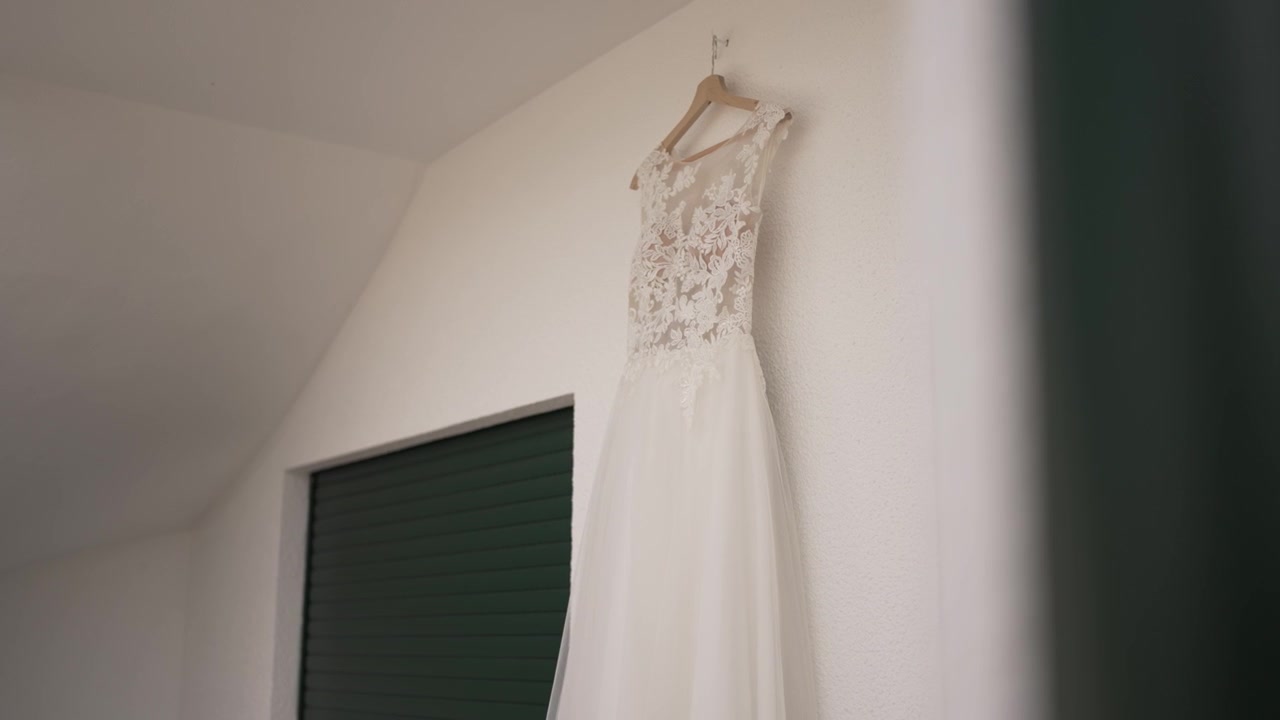 Lace wedding dress hanging on a wooden hanger against a white wall