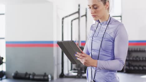 video of concentrating caucasian female fitness trainer using tablet at a gym