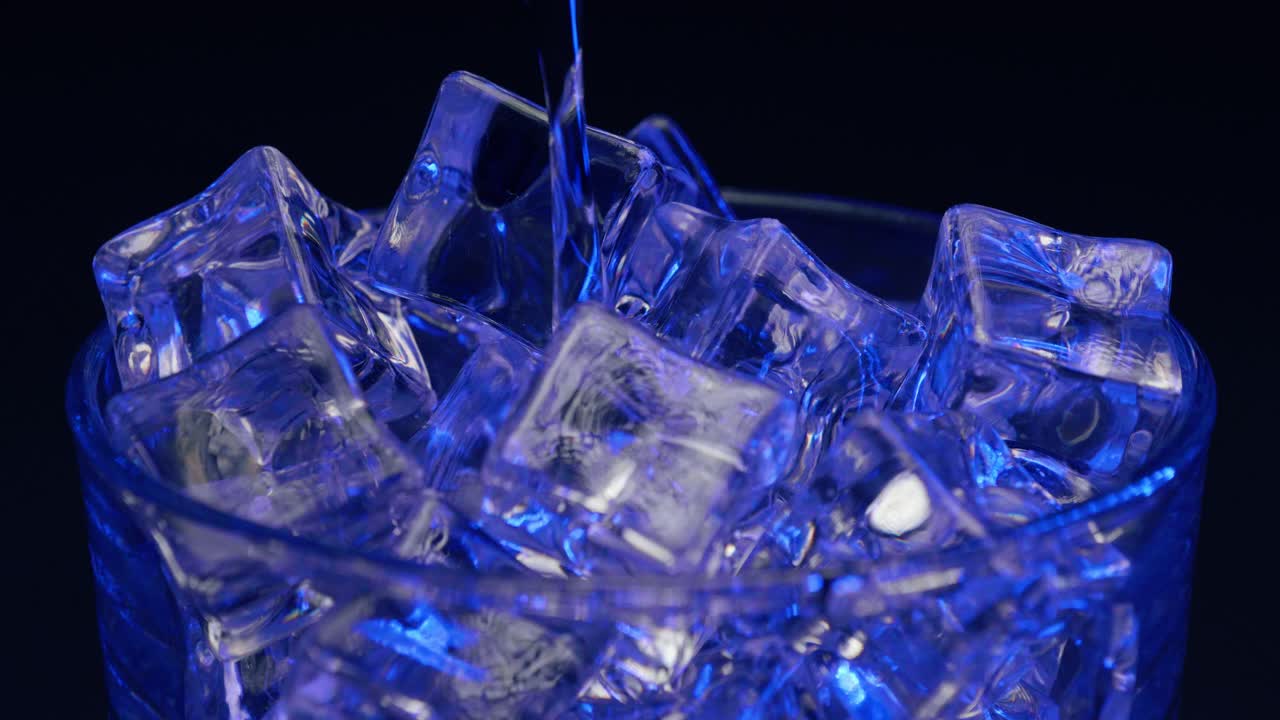 푸른 빛과 채색이 있는 예술적인 칵테일의 정적인 샷이 검은색 배경, 장식 없이 바위에 있는 얼음 위에 부어지고 있습니다.