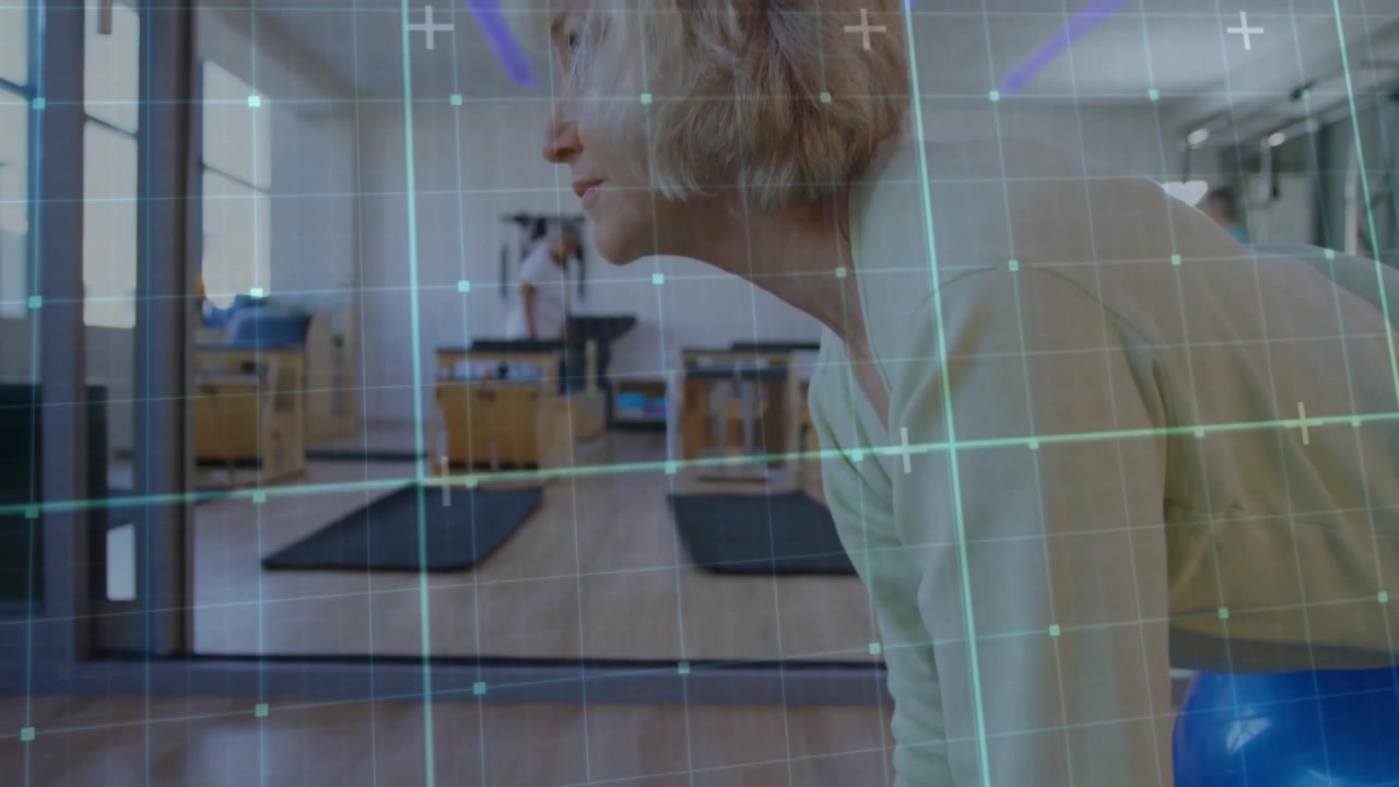 Senior woman balancing on blue stability ball in pilates studio, showing gridded overlay lines