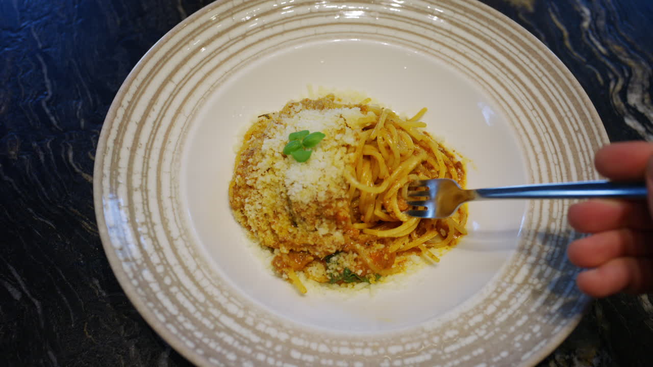 Primo piano di una forchetta che solleva pasta ricoperta di formaggio grattugiato da un piatto in un ristorante