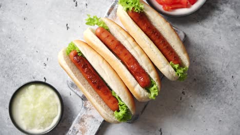 Three-barbecue-grilled-hot-dogs-with-sausage-placed-on-wooden-cutting-board