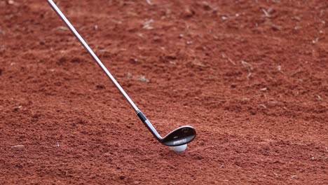 golf club hitting ball, creating a sand trail.