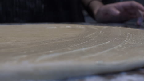 female hands spreading melted butter on flattened pastry dough on table