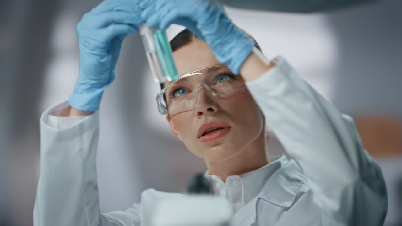 Primo piano di un biochimico professionista con occhiali che esamina una provetta con medicinali.