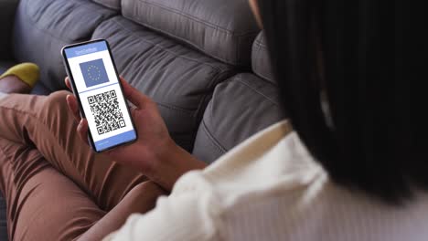 Woman-at-home-holding-smartphone-with-covid-vaccination-certificate,-eu-flag-and-qr-code-on-screen