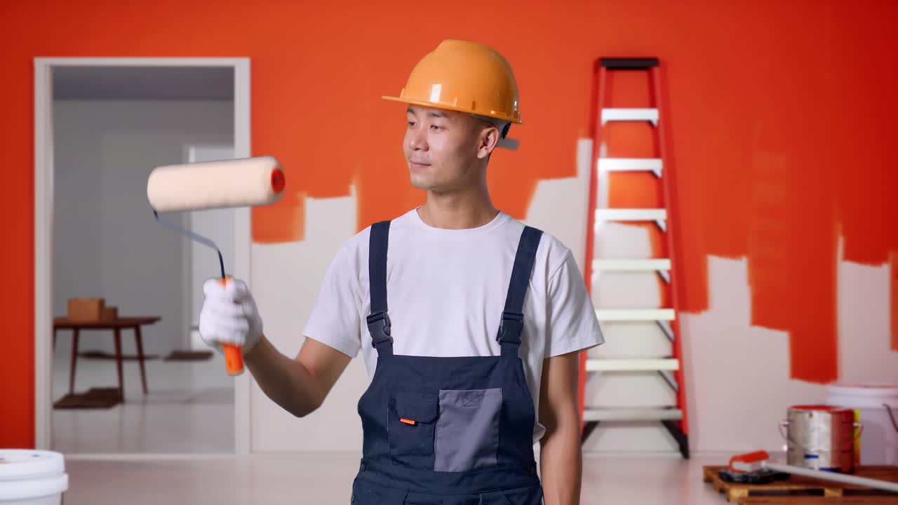 pintor hombre asiático con casco de seguridad pintando y sonriendo con pintura pared en la habitación